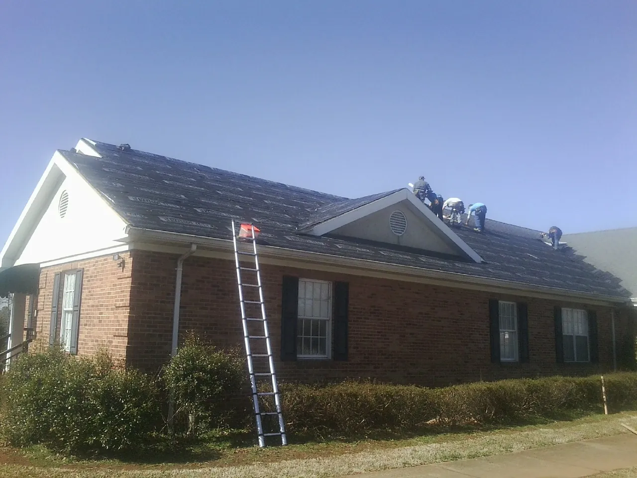 Crew tearing shingles off a brick ranch roof with a ladder set — Emergency Roof Repair work by our crew in Temple